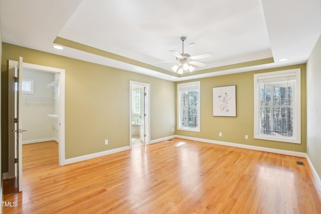 empty room featuring plenty of natural light, baseboards, light wood-style floors, and a tray ceiling