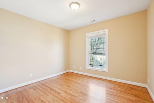 spare room featuring light wood finished floors, visible vents, and baseboards