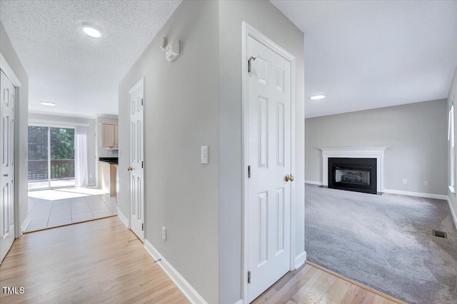 corridor with baseboards, visible vents, light colored carpet, a textured ceiling, and light wood-style floors