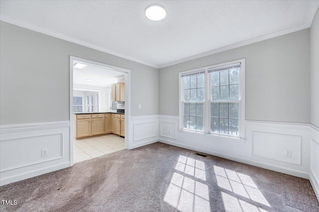 unfurnished room with a wainscoted wall, light colored carpet, crown molding, and visible vents