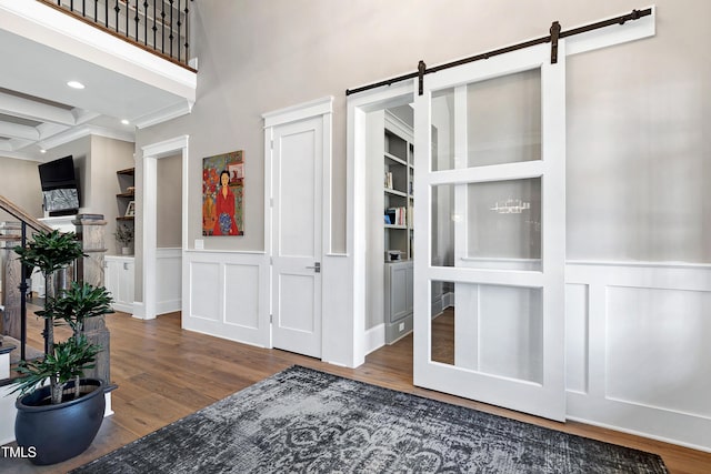 interior space featuring a barn door, a wainscoted wall, stairway, wood finished floors, and beam ceiling