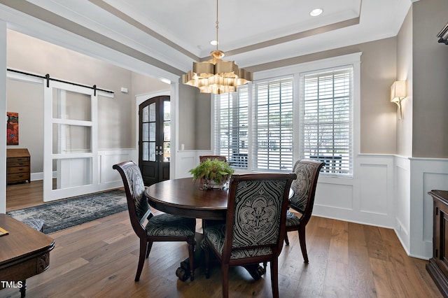 dining area with wood-type flooring, a barn door, a raised ceiling, and french doors