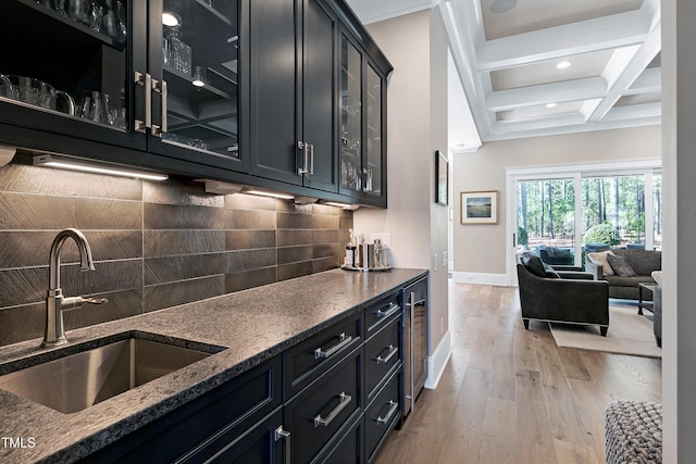 kitchen with dark cabinetry, light wood-style flooring, decorative backsplash, a sink, and coffered ceiling