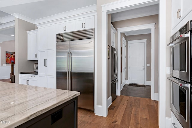 kitchen featuring light stone counters, crown molding, appliances with stainless steel finishes, white cabinetry, and wood finished floors