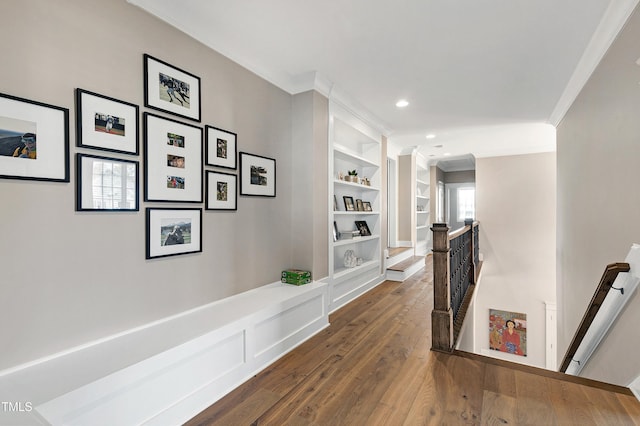 corridor featuring built in features, dark wood-style flooring, crown molding, and an upstairs landing