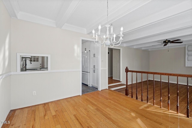 spare room with ceiling fan with notable chandelier, a sink, wood finished floors, ornamental molding, and beamed ceiling