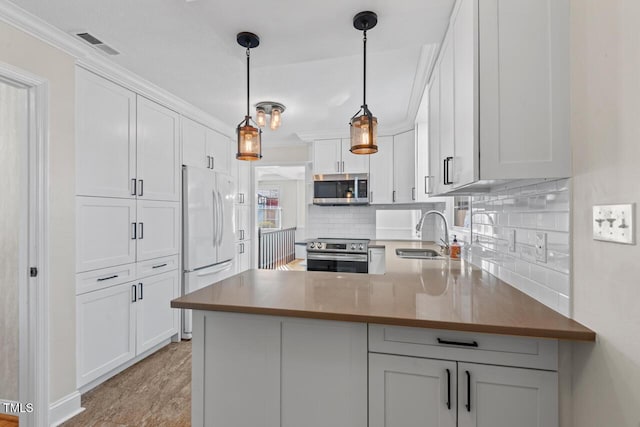 kitchen featuring stainless steel appliances, a peninsula, a sink, white cabinets, and hanging light fixtures