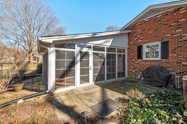 rear view of property with brick siding, a sunroom, and a patio