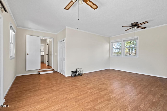 empty room with a textured ceiling, ceiling fan, light wood-type flooring, and crown molding