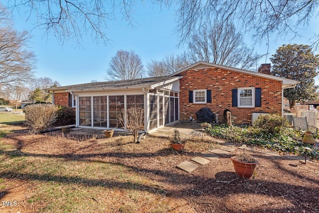 back of house featuring a sunroom, brick siding, and a chimney