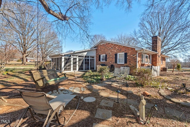 rear view of property featuring a sunroom, a chimney, central AC unit, and brick siding