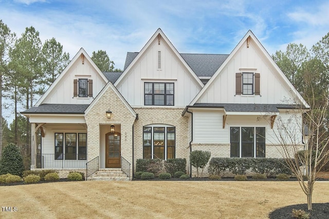 view of front of property with covered porch, brick siding, board and batten siding, and a shingled roof