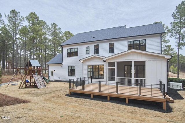 back of house featuring a sunroom, roof with shingles, a wooden deck, a playground, and board and batten siding