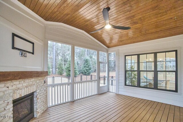 unfurnished sunroom with vaulted ceiling, ceiling fan, a fireplace, and wood ceiling