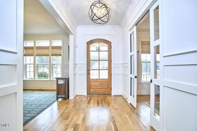 entryway featuring crown molding, light wood finished floors, an inviting chandelier, and a decorative wall