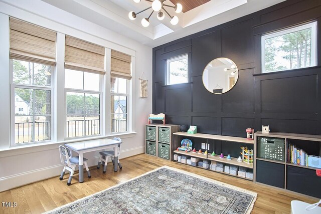 rec room with a chandelier, a tray ceiling, a decorative wall, and wood finished floors