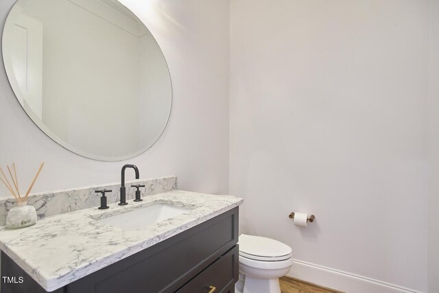 half bathroom featuring toilet, wood finished floors, vanity, and baseboards