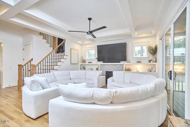 living room with stairway, light wood-style floors, ceiling fan, coffered ceiling, and beamed ceiling