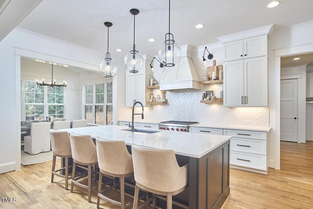 kitchen with open shelves, light countertops, white cabinets, a sink, and an island with sink