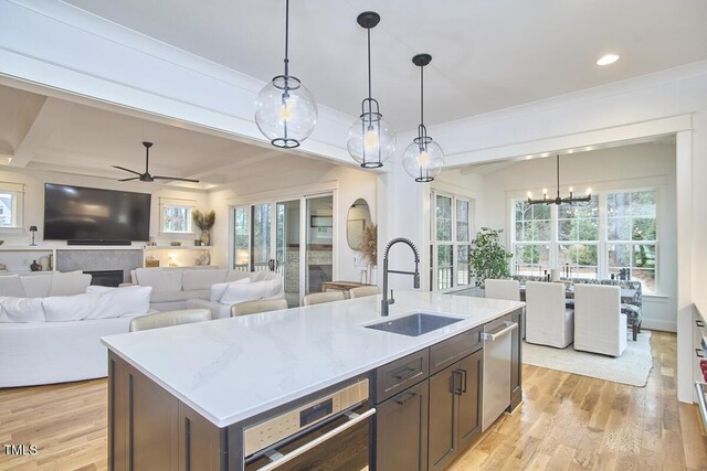 kitchen featuring open floor plan, a kitchen island with sink, light wood-style floors, pendant lighting, and a sink