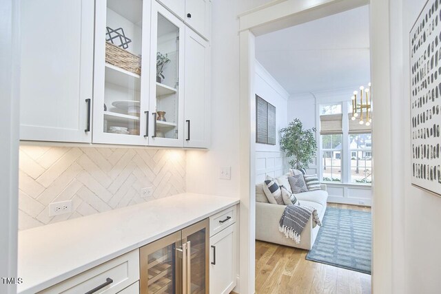 bar featuring beverage cooler, light wood-style floors, backsplash, decorative light fixtures, and crown molding