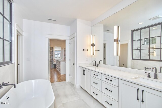 full bath featuring visible vents, a sink, a freestanding bath, and double vanity