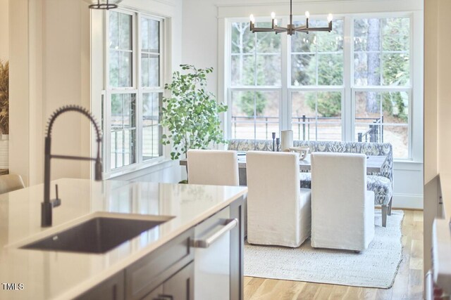 kitchen featuring light countertops, stainless steel dishwasher, an inviting chandelier, light wood-style floors, and a sink