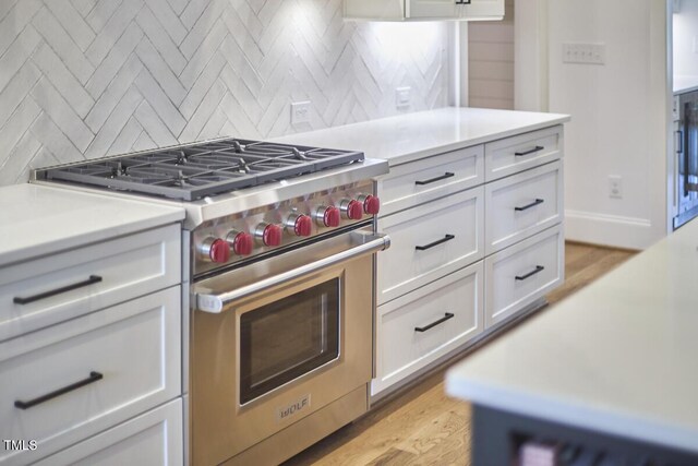 kitchen with tasteful backsplash, light countertops, white cabinetry, and premium range