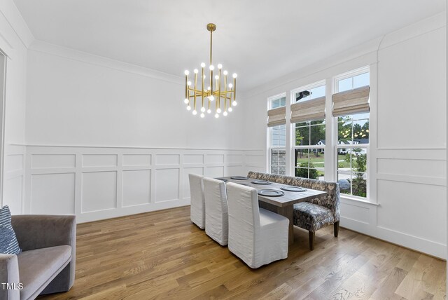 dining room featuring crown molding, light wood finished floors, a decorative wall, and a notable chandelier