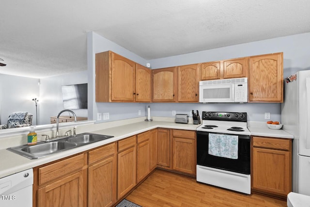 kitchen featuring white appliances, light countertops, a textured ceiling, light wood-type flooring, and a sink