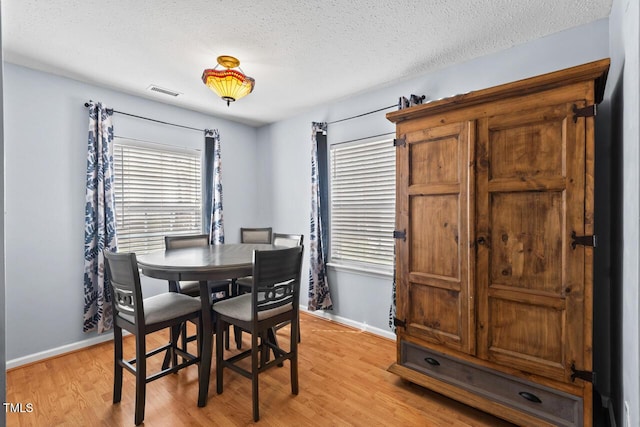 dining space with baseboards, visible vents, a textured ceiling, and light wood finished floors