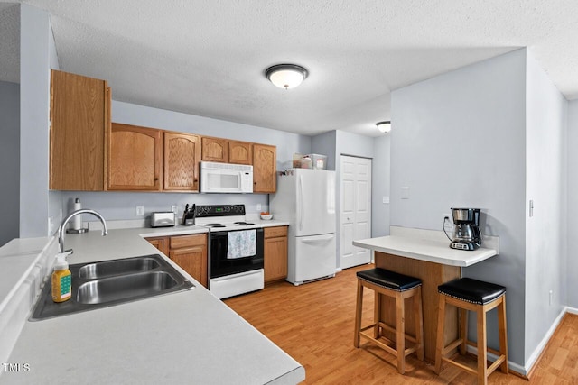 kitchen with a breakfast bar, light countertops, a sink, light wood-type flooring, and white appliances