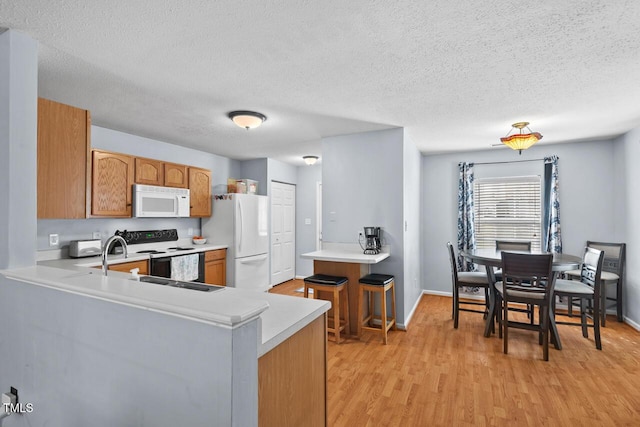 kitchen featuring light wood-style flooring, a peninsula, white appliances, light countertops, and brown cabinets