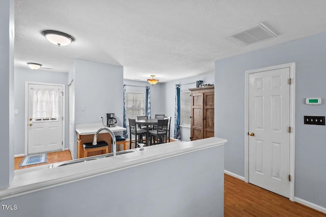 kitchen featuring a textured ceiling, a sink, wood finished floors, visible vents, and baseboards