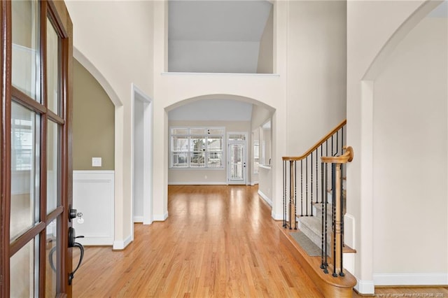 entryway featuring arched walkways, a wainscoted wall, a towering ceiling, stairs, and light wood finished floors