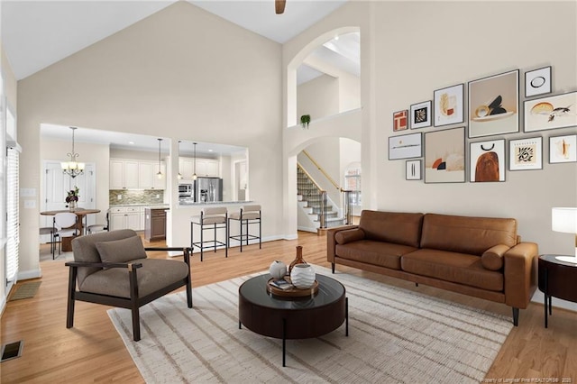 living area featuring visible vents, arched walkways, light wood-style flooring, stairway, and a notable chandelier