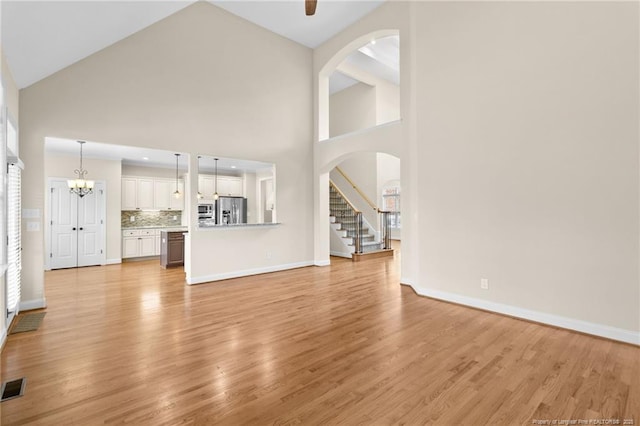 unfurnished living room featuring high vaulted ceiling, light wood-style flooring, visible vents, baseboards, and stairs