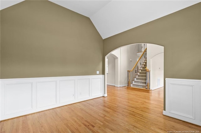 empty room with light wood-type flooring, arched walkways, vaulted ceiling, and stairs