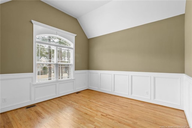 spare room featuring light wood-type flooring, wainscoting, visible vents, and vaulted ceiling