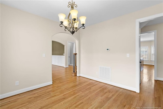 empty room with arched walkways, visible vents, a chandelier, light wood-type flooring, and baseboards