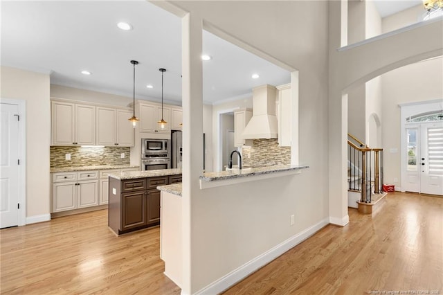 kitchen featuring pendant lighting, custom exhaust hood, stainless steel appliances, light stone countertops, and a peninsula