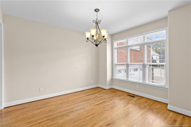 spare room featuring visible vents, light wood-style flooring, baseboards, and an inviting chandelier