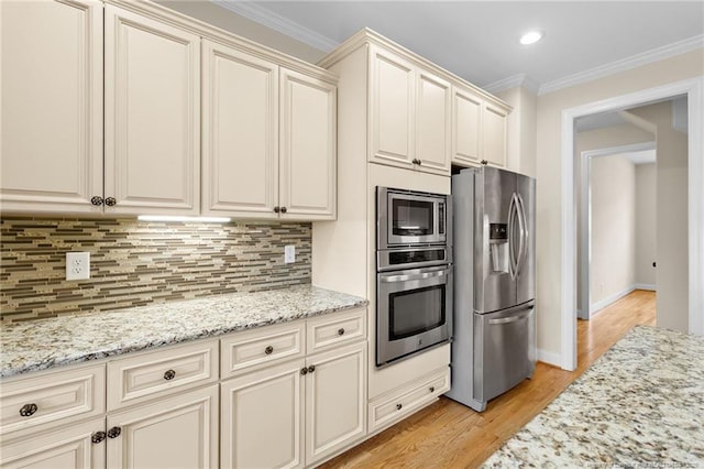 kitchen with light stone countertops, cream cabinets, stainless steel appliances, crown molding, and backsplash