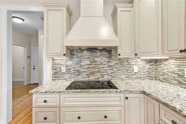 kitchen with light stone countertops, custom range hood, black electric stovetop, and decorative backsplash