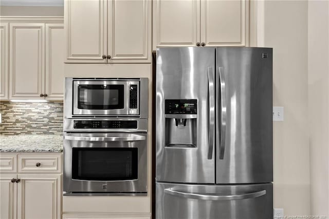 kitchen featuring cream cabinets, light stone counters, stainless steel appliances, and decorative backsplash