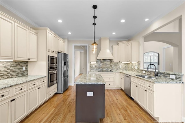 kitchen with decorative light fixtures, custom exhaust hood, stainless steel appliances, a sink, and a peninsula