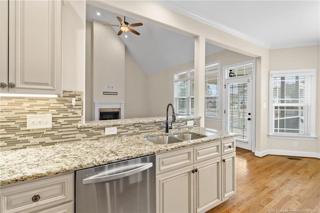 kitchen with a sink, light wood-style floors, stainless steel dishwasher, backsplash, and light stone countertops