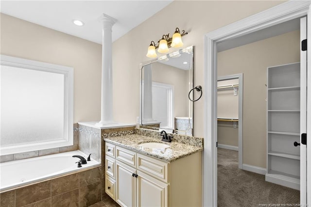 full bath featuring decorative columns, baseboards, a garden tub, a spacious closet, and vanity