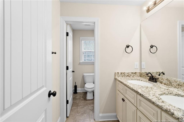 full bathroom with double vanity, a sink, toilet, and baseboards