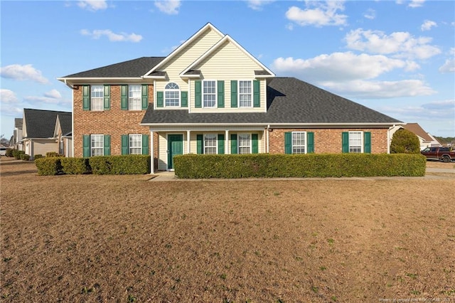 view of front of property featuring a shingled roof, brick siding, and a front lawn